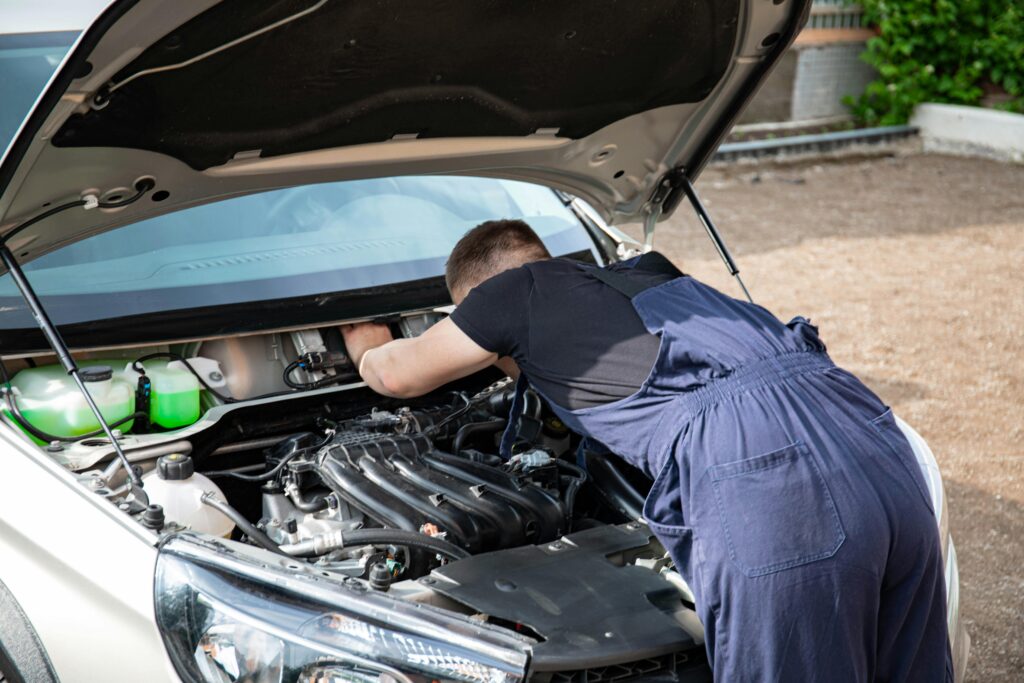 Mechanic repairing car engine in daylight, showcasing technical skills.